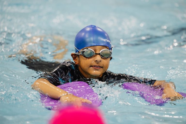 Girl swims with swimming hat, goggles and two floats as part of swimming lesson