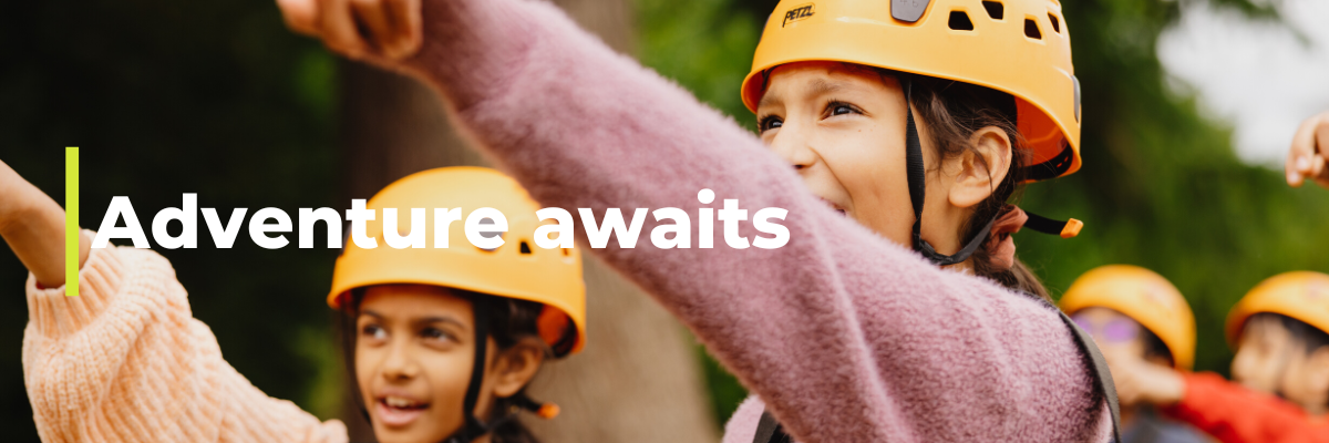 Two young girls in helmets point towards high ropes outdoor activity 